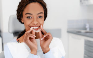 A woman at the dentist smiling while holding her clear braces.