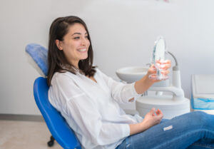 Young Woman Looking At Mirror after Dental Implants
