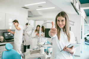 Young Beautiful Dentist Posing With Thumb Up in Crowded Clinic