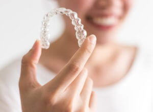 A smiling woman holding invisalign or invisible braces, orthodontic equipment