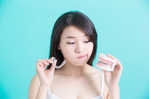 A young lady holds both Clear Braces and Metal Braces in her hands, unsure which one to choose.