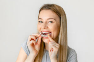 Teenage girl using invisible braces putting her clear aligners in her mouth.