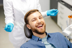Image of a happy man sitting in a dentist's chair at a modern clinic and smiling while receiving dental care.