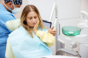 Young woman experiencing pain while holding her cheek in a dentist's office due to a dental emergency.