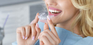 An image of a female patient holding clear, invisible braces to insert into her mouth.