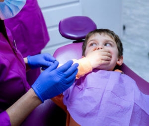 A boy at the dentist's office covers his mouth in fear during an emergency dental visit.