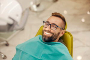 A portrait of a patient sitting in a dentist's chair with a perfect smile after teeth whitening.