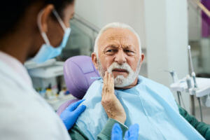 Senior man complaining about toothache to his dentist during appointment at dentist's office.