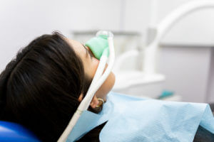 An adult woman sits in a dentist's clinic wearing a nasal mask to inhale nitrous oxide for dental sedation.