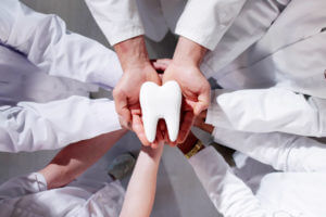 Group Of Dentists Holding Tooth Which Symbolizes Dental Care.